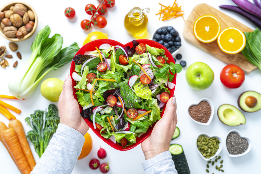 Hands holding a red bowl full of salad surrounded by plant-based foods