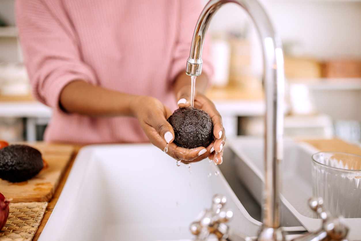Close up of woman's hands washes a avocado under water in a domestic kitchen