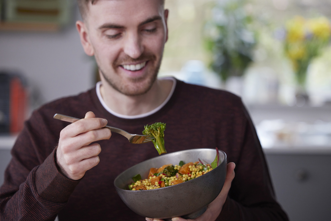 Close Up Of Man Eating Healthy Vegan Lunch In Kitchen At Home