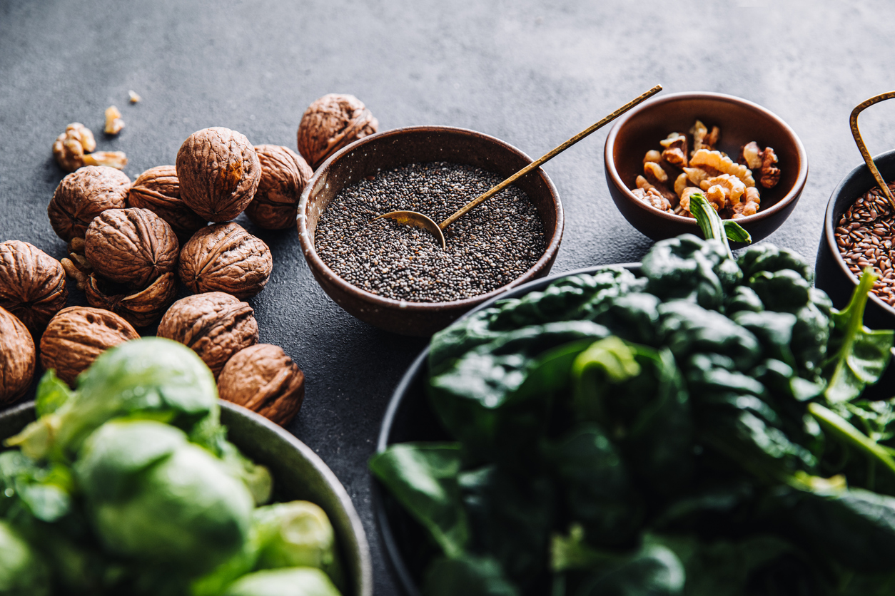 Close-up of omega 3 vegan food in bowls on black table. Fresh green spinach, flax seeds, walnuts,  and brussel sprouts in bowls on a table.