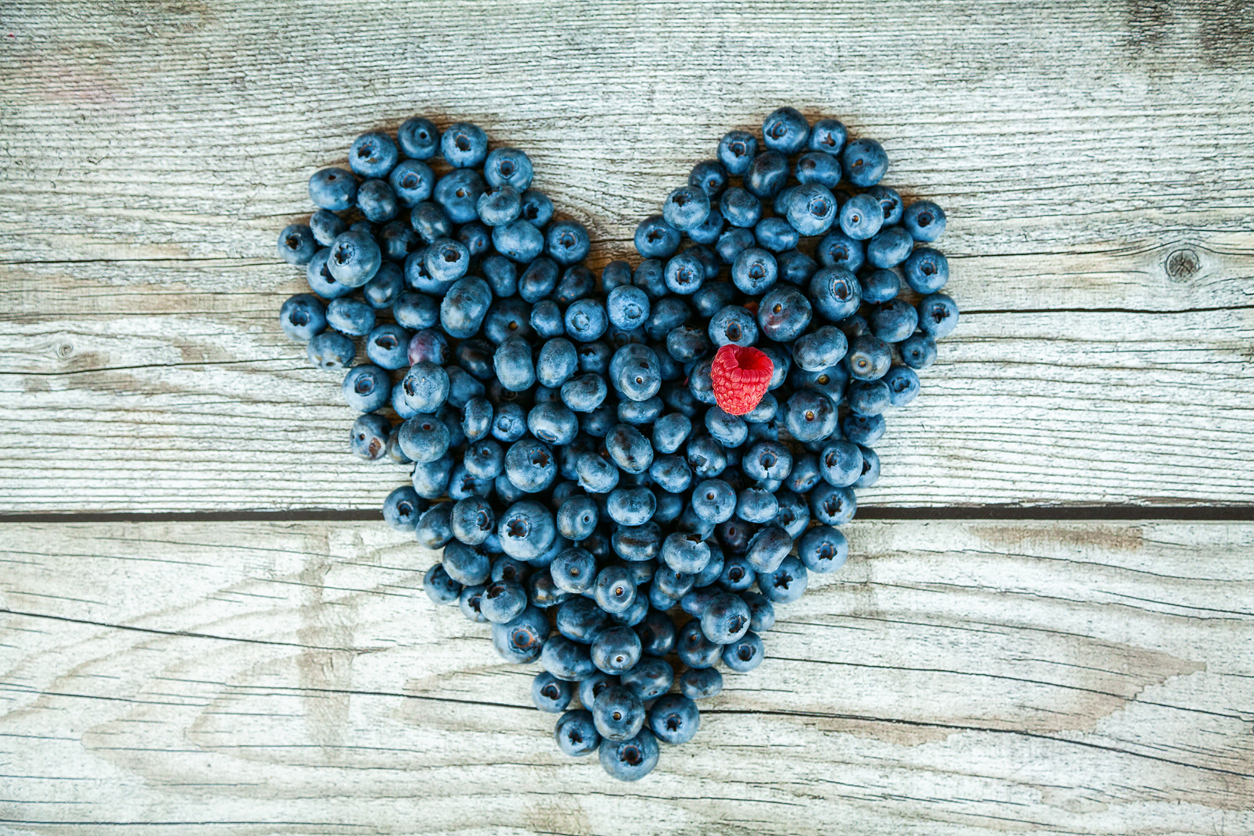 Heart shaped blueberries with one raspberry on a gray wooden background