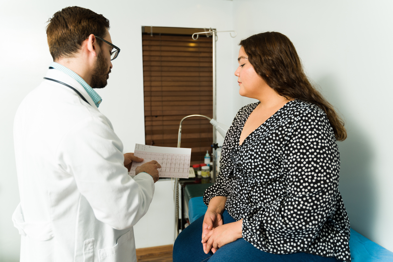 Cardiologist showing and explaining the electrocardiogram results to an overweight young woman with heart problems