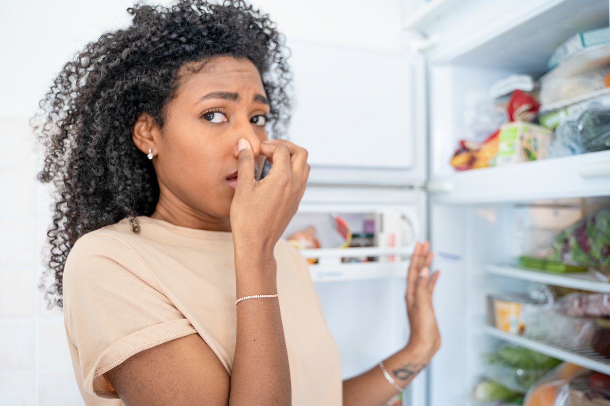 One disgusted black woman smelling stinky and dirty fridge