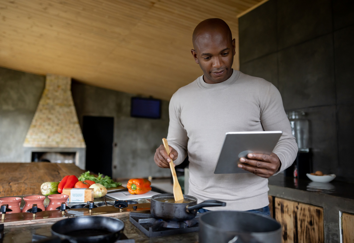 Happy man cooking at home following an online recipe on a tablet - domestic life concepts