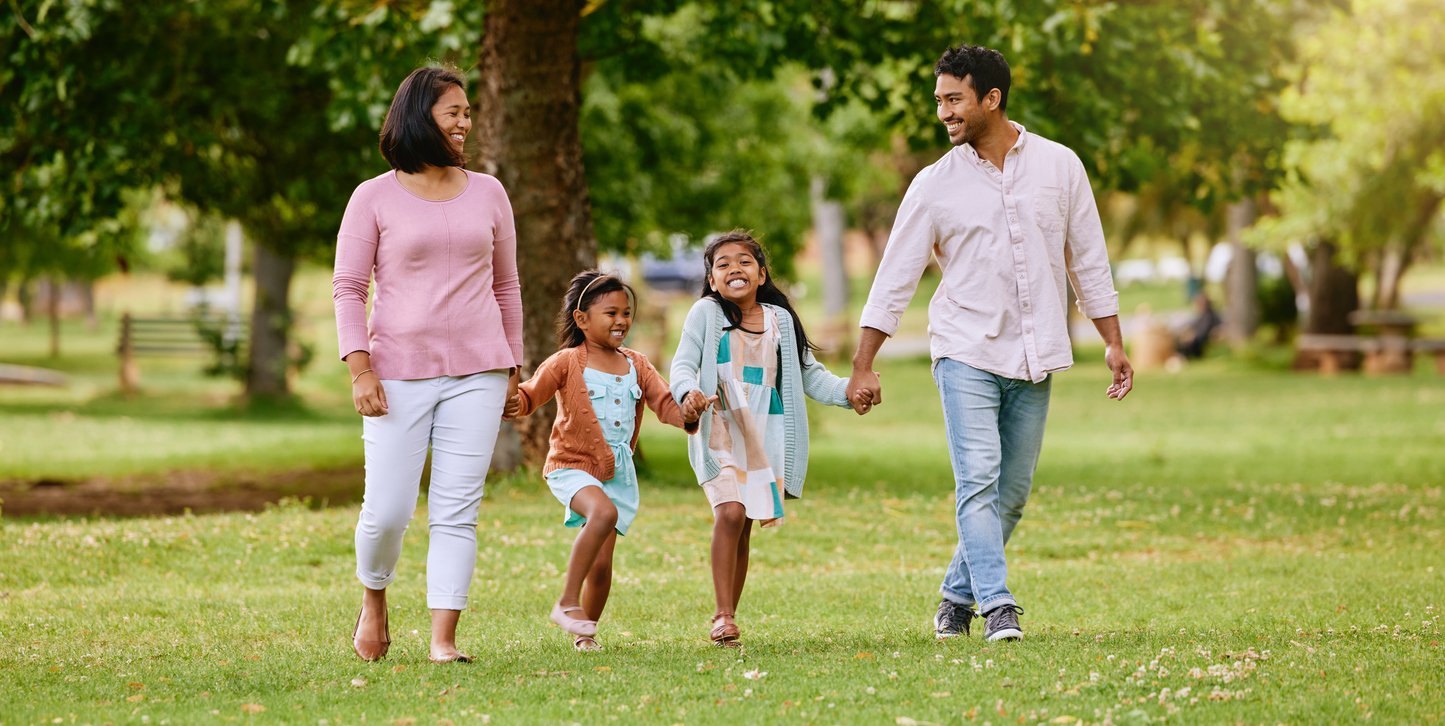 Young happy mixed race family holding hands and walking together in a park. Loving parents spending time with their little daughters in nature. Sisters bonding with their mom and dad outside