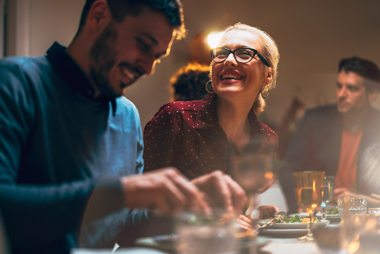 Happy friends talking and laughing together while sitting at dinner table and eating delicious food.