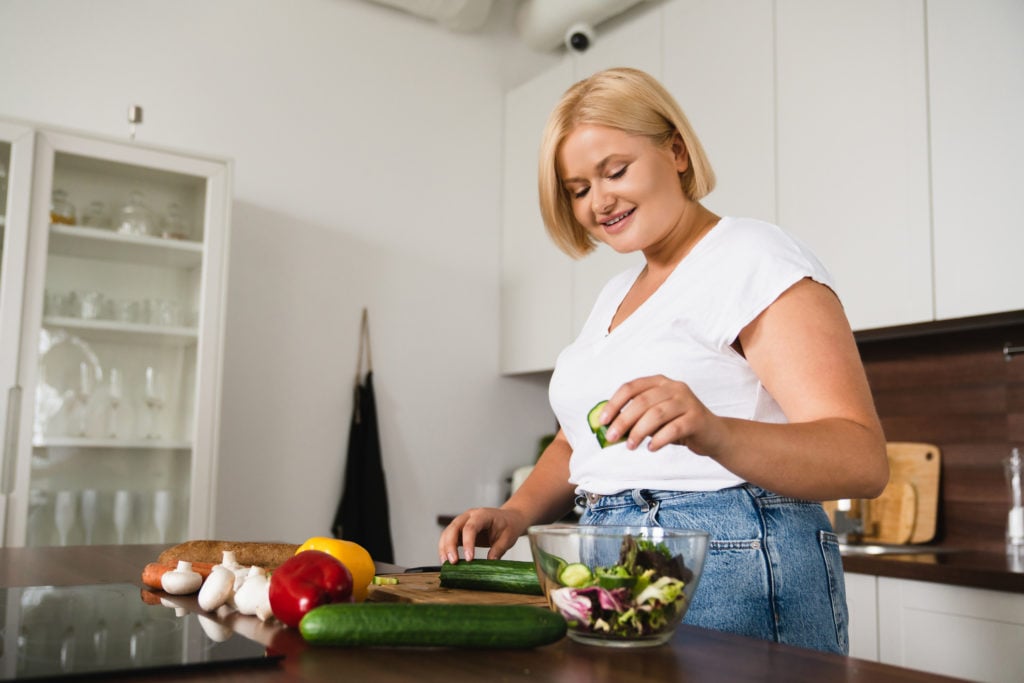 Young caucasian woman preparing a fiber-rich salad in the kitchen