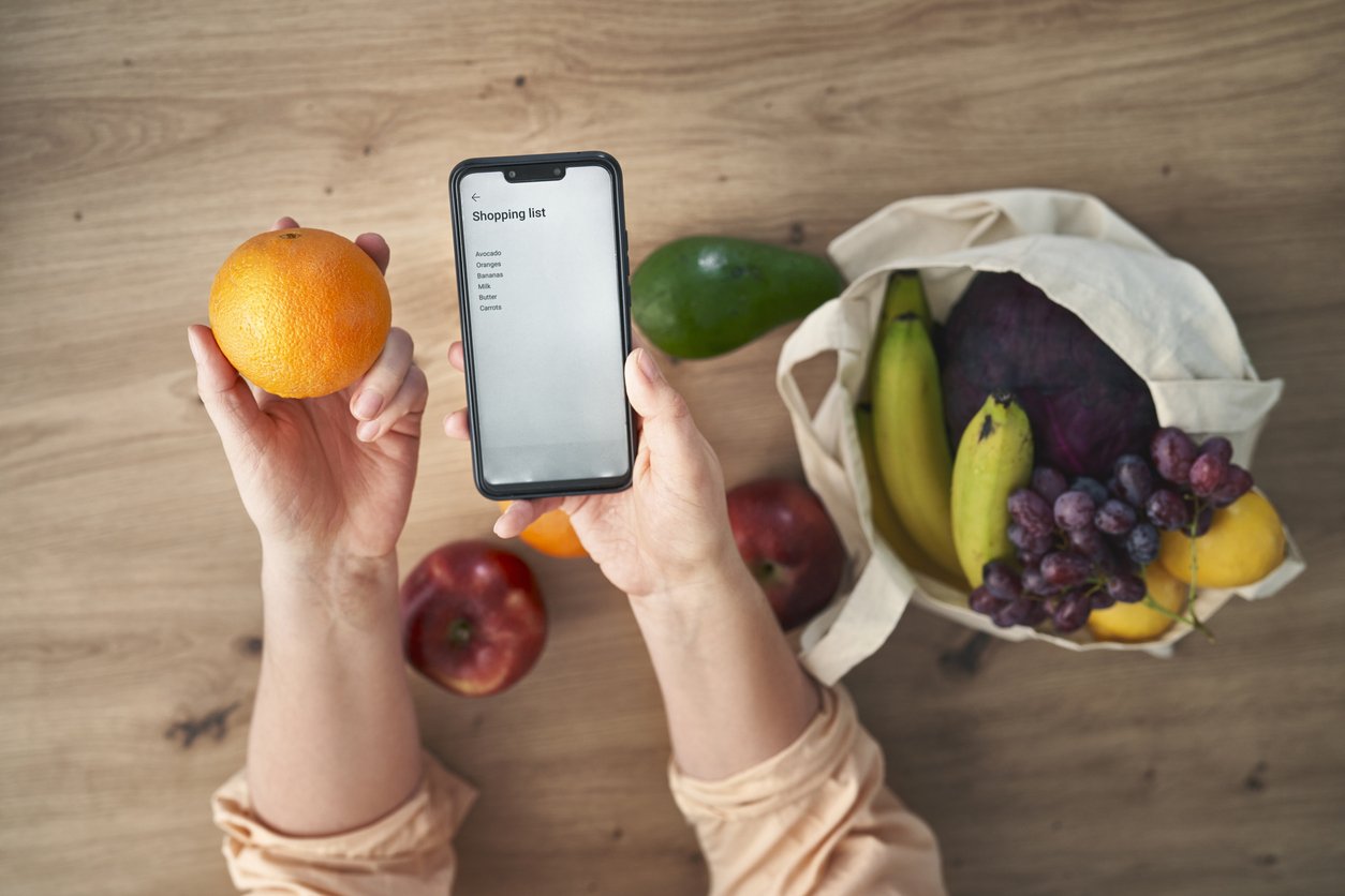 Woman holding phone with shopping list and some fruits