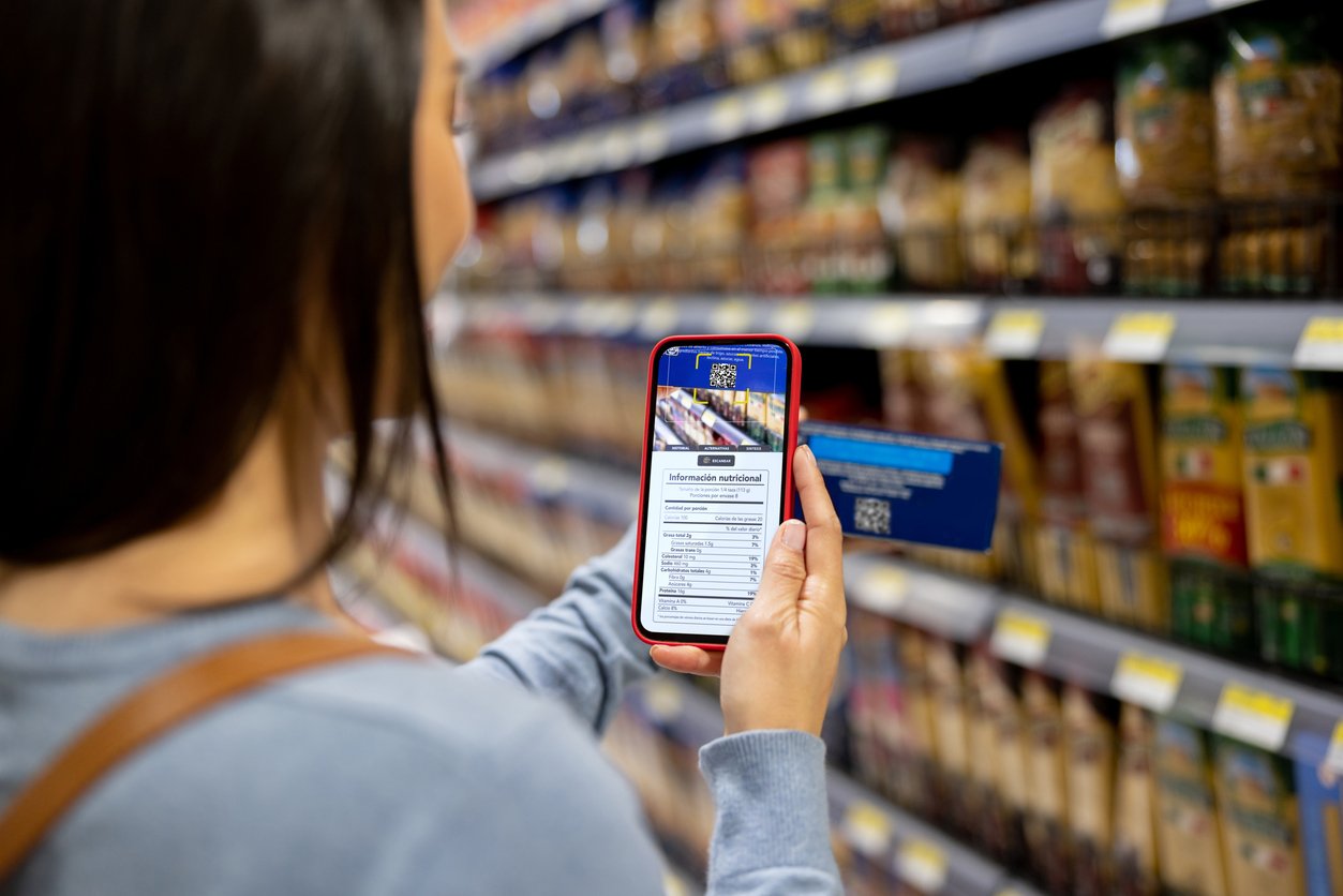 Close-up on a woman shopping at the supermarket and scanning a product label with her cell phone â healthy eating concepts