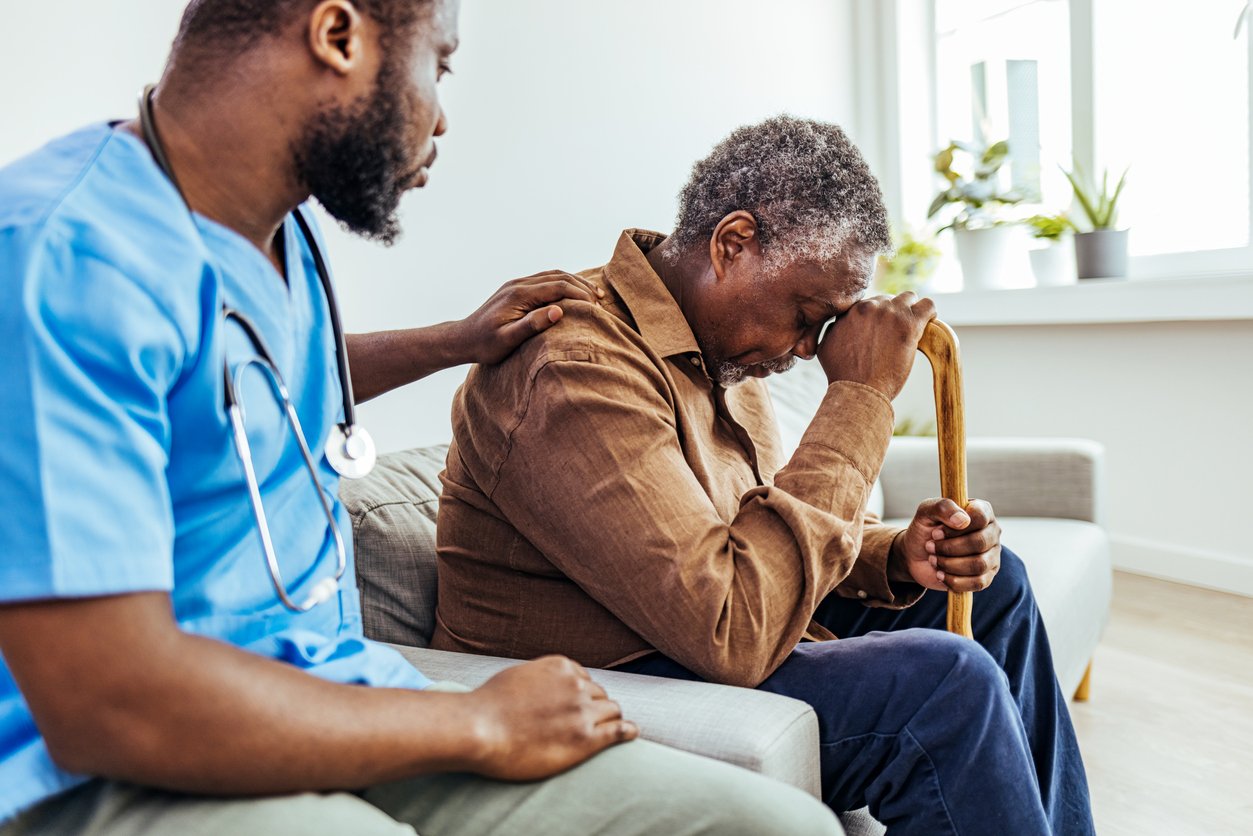 Male professional doctor touching shoulder, comforting upset senior patient.