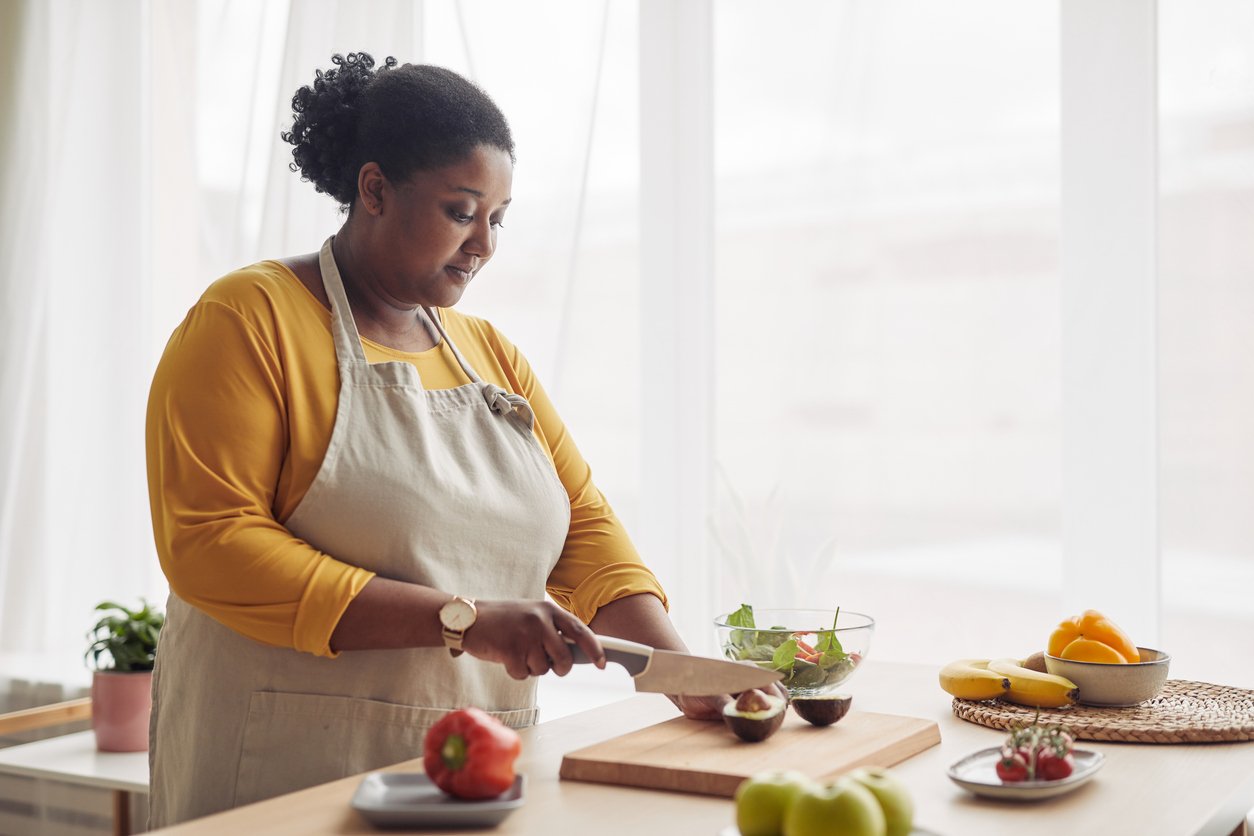 Black woman cutting fresh fruits and vegetables in the kitchen