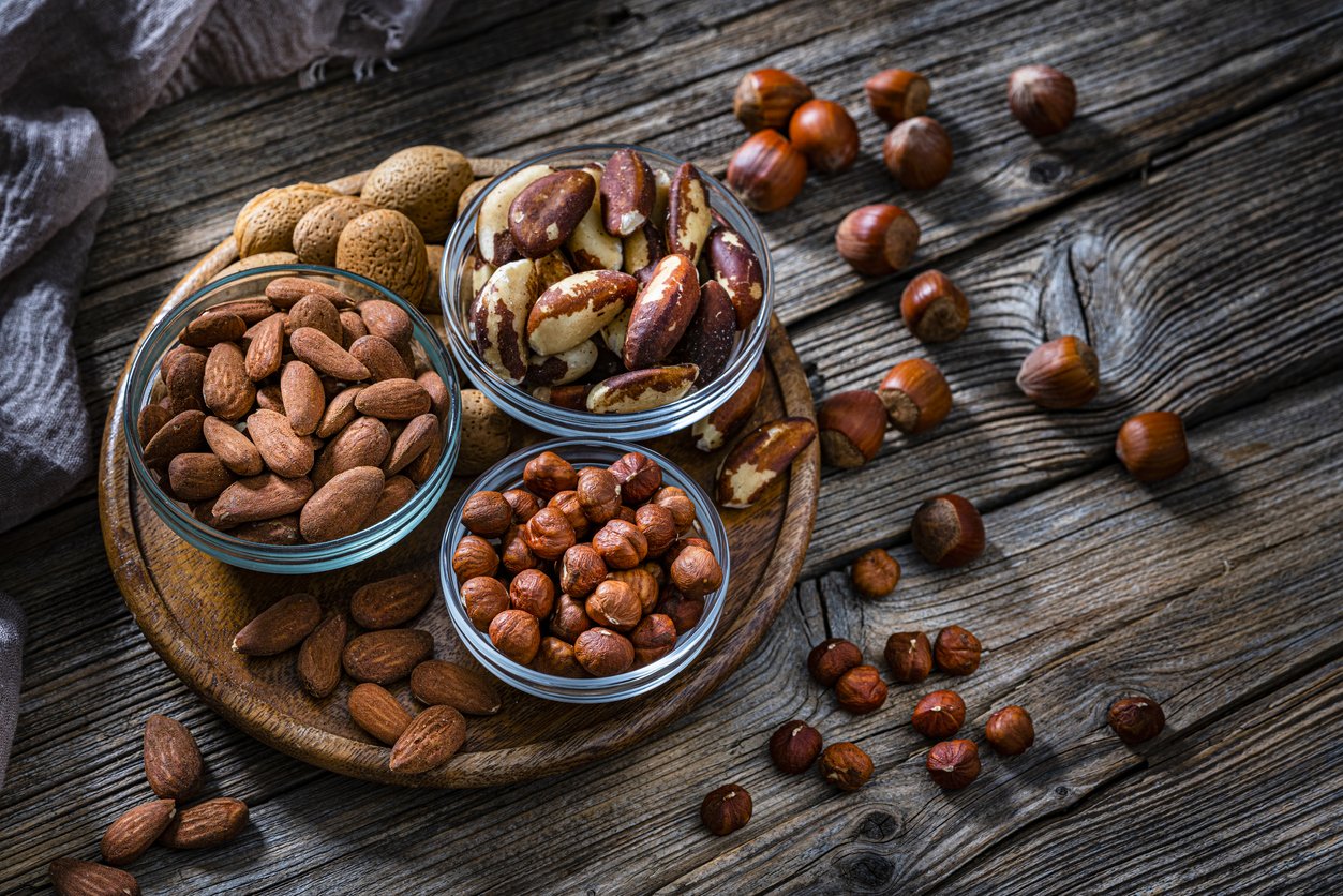 High angle view of three bowls filled with hazelnuts, almonds and Brazil nuts shot on dark rustic table. Some nuts are out the bowls spilled on the table