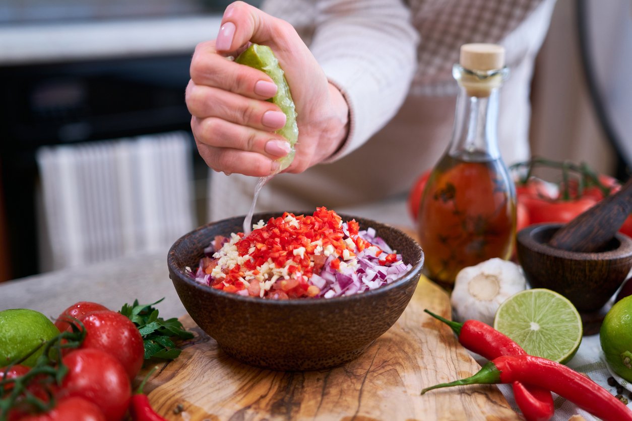 making salsa dip sauce - woman squeezing fresh lime juice to chopped ingredients in wooden bowl.