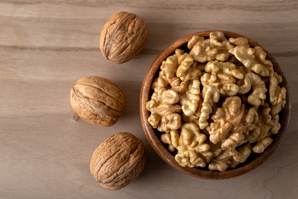 Shelled walnuts and whole walnuts on wooden background