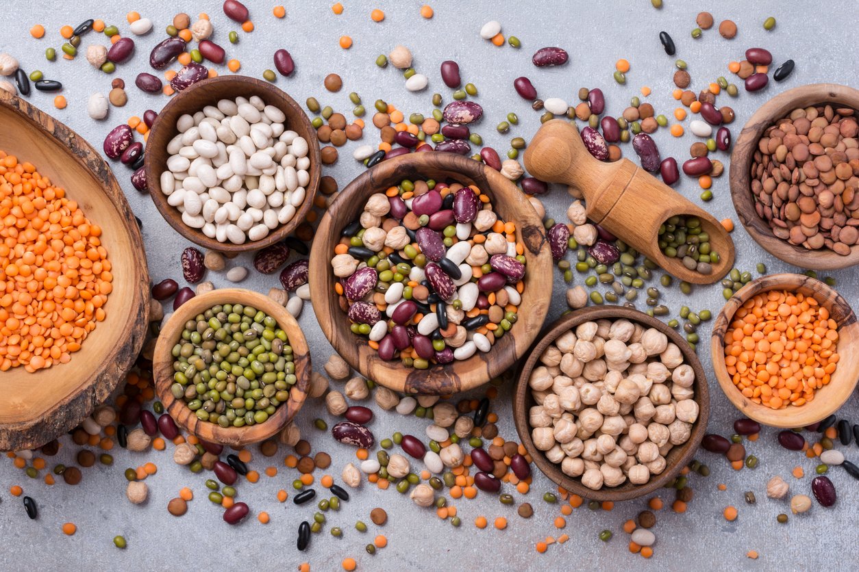 Top view of different beans, lentils, mung, chickpeas in wooden bowls for tasty meals on grey concrete background