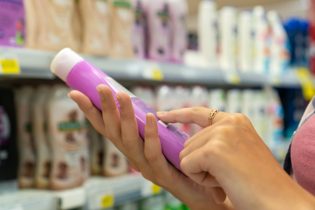 Close-up of a young woman's hands reading information on a bottle of shower gel in a store. Buying cosmetics in the store. Shopping trip.