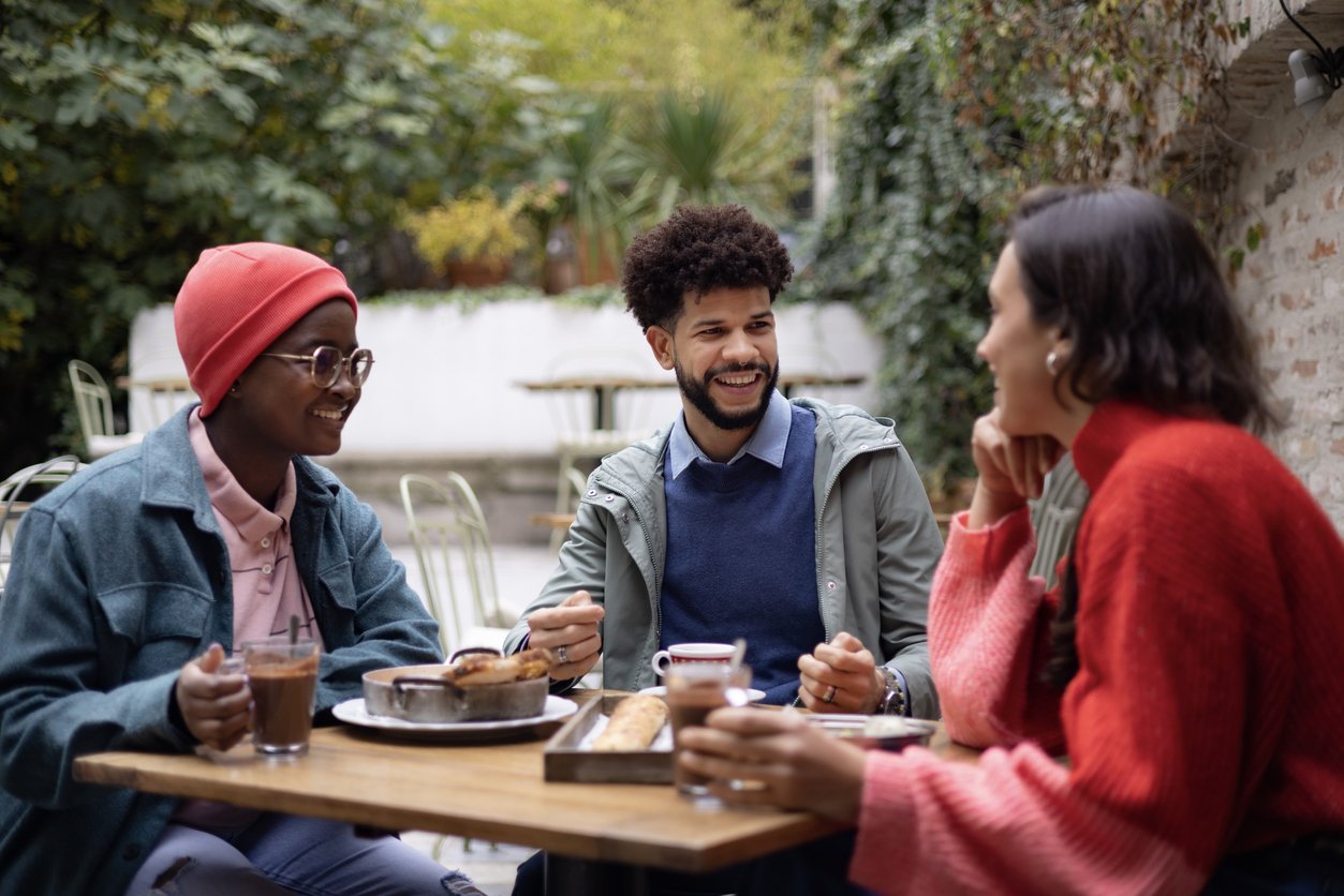 A small happy diverse group of friends meeting in a local outdoor restaurant, sitting at the table and having a meal together