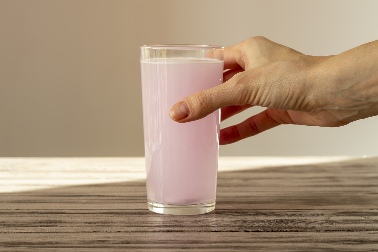 The pink electrolyte tablet dissolves in water. The woman's hand holds a glass of fizzy water with vitamin C