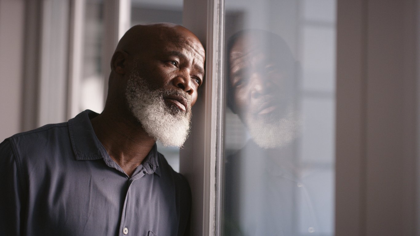 Sad, depression or black man burnout at window with mental health, headache or anxiety in house. Lonely, stress or depressed man thinking for financial problem, health compliance or finance policy