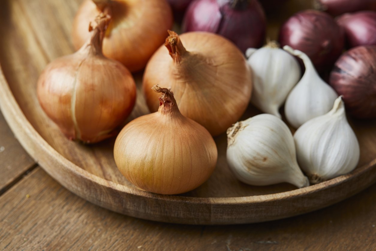 Garlic, onion and Spanish onion on a wooden plate, seasoning vegetables on a wooden kitchen table top, a top view with a copy space area