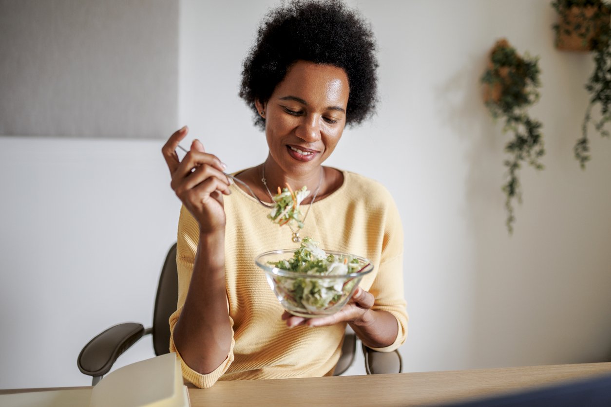 Mid adult black woman having snack at home office