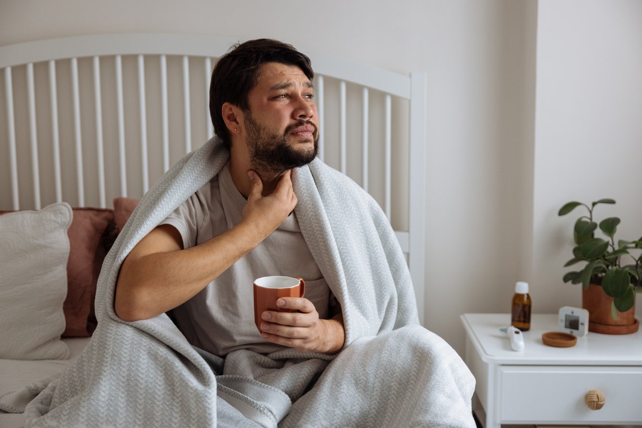 Close up young man using hand for touching neck with feeling sore throat after wake up in the morning at bedroom , health care lifestyle people concept