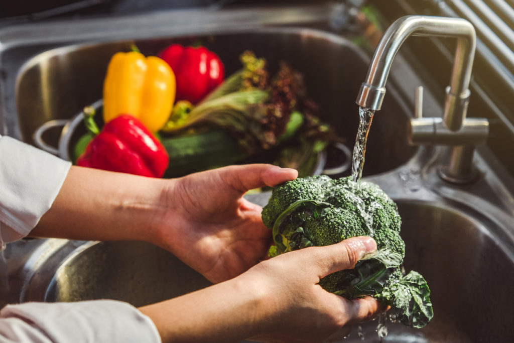 Hands washing fresh vegetables in a sink