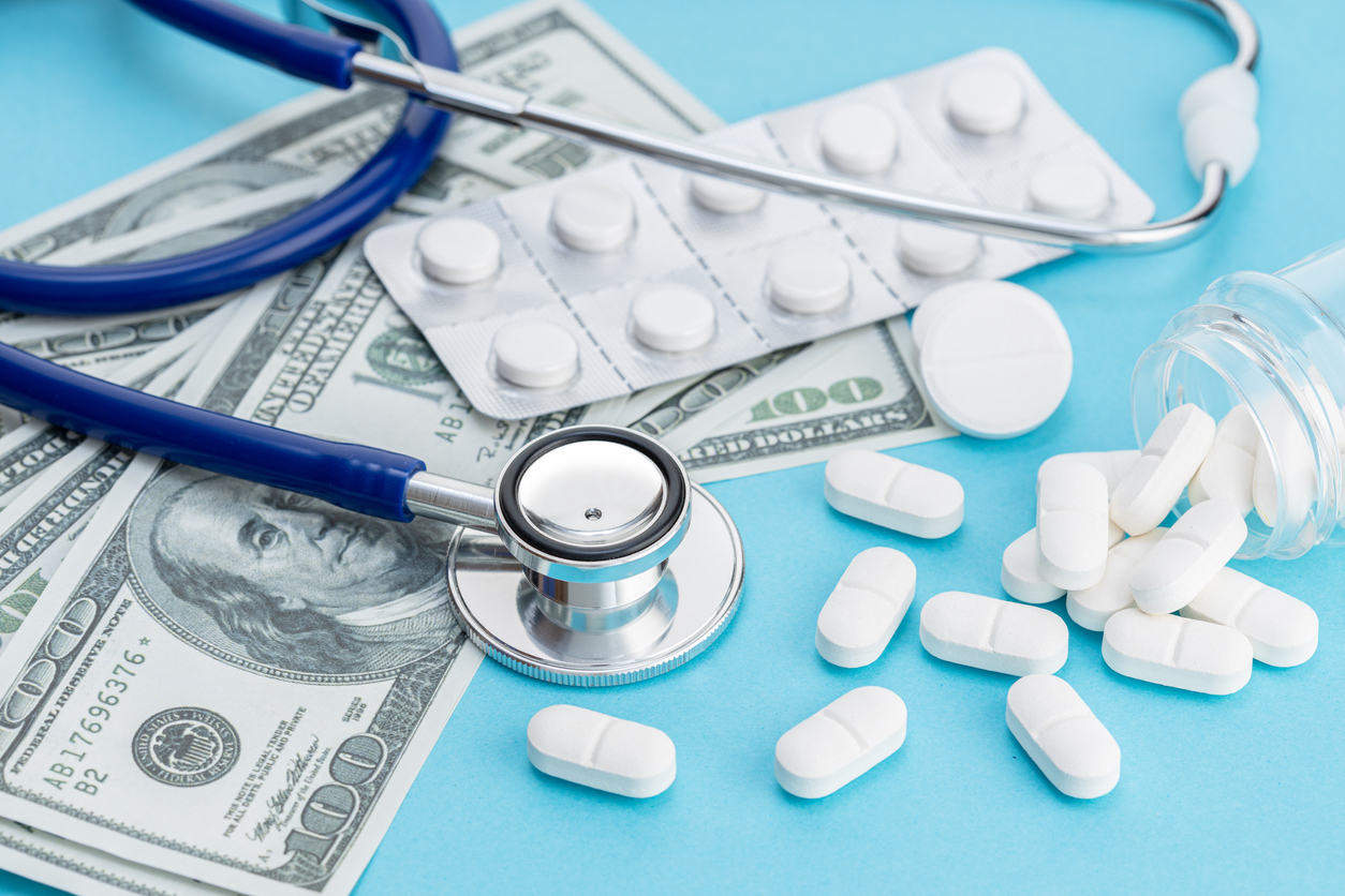 Healthcare cost concept. US Dollars bills, stethoscope and medicine pills on blue background