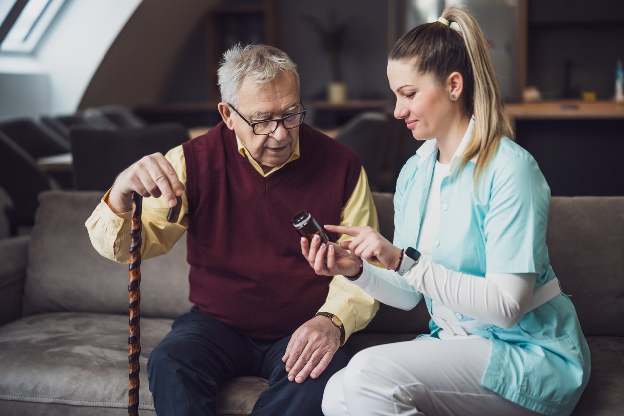 Nurse home caregiver is assisting old man at his home. Professional health support for elderly people.