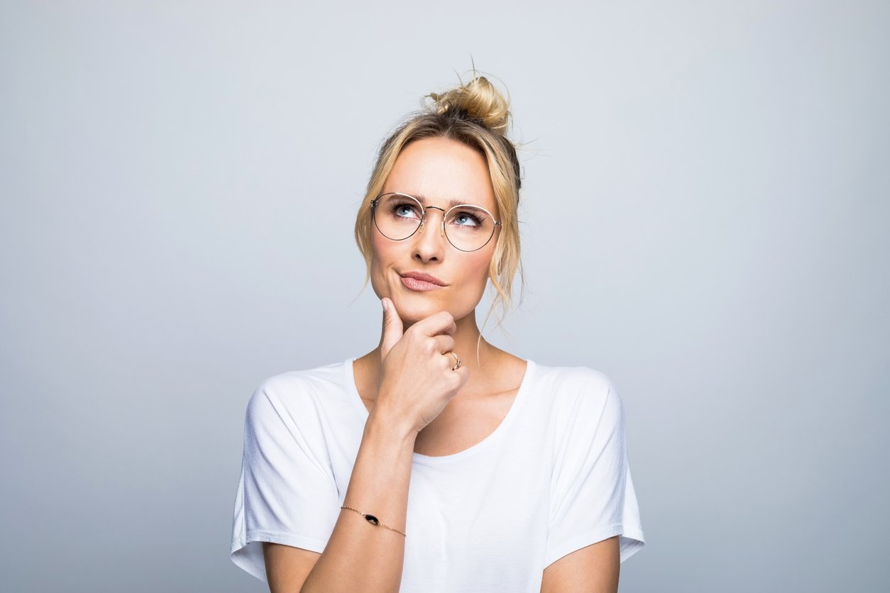 Thoughtful blond woman with hand on chin looking up against gray background