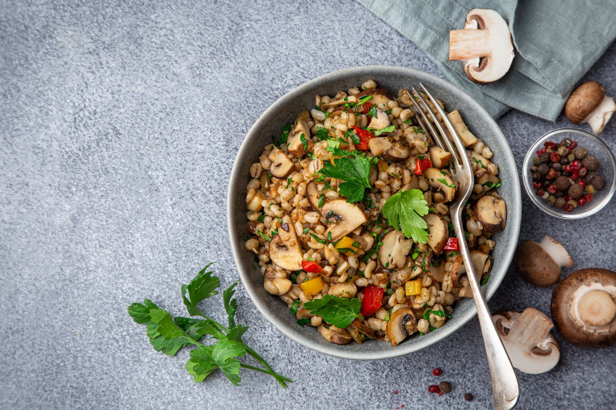 Warm pearl barley salad with mushrooms and vegetables, top view, copy space