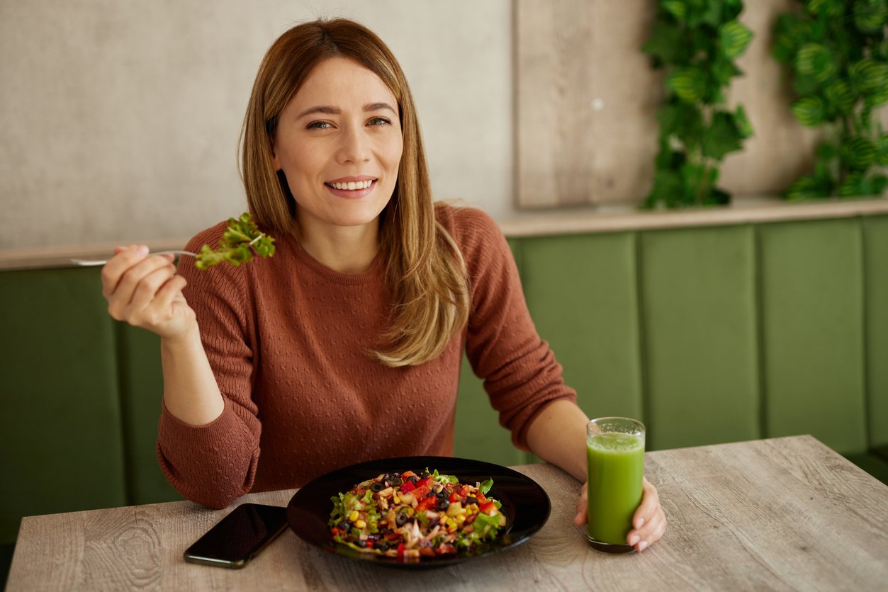 Mid adult woman enjoys eating salad and drinking smoothie in salad bar