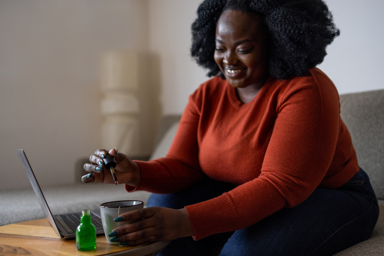 Happy black woman enjoying free time at home and relaxing with herbal cannabis oil drops