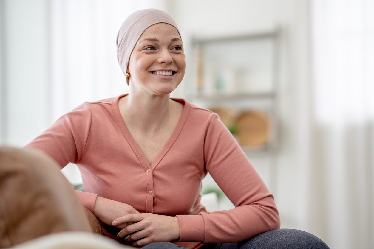 A young woman battling cancer sits in the comfort of her own home between treatments as she poses for a portrait.  She is dressed comfortably and wearing a headscarf to keep warm.