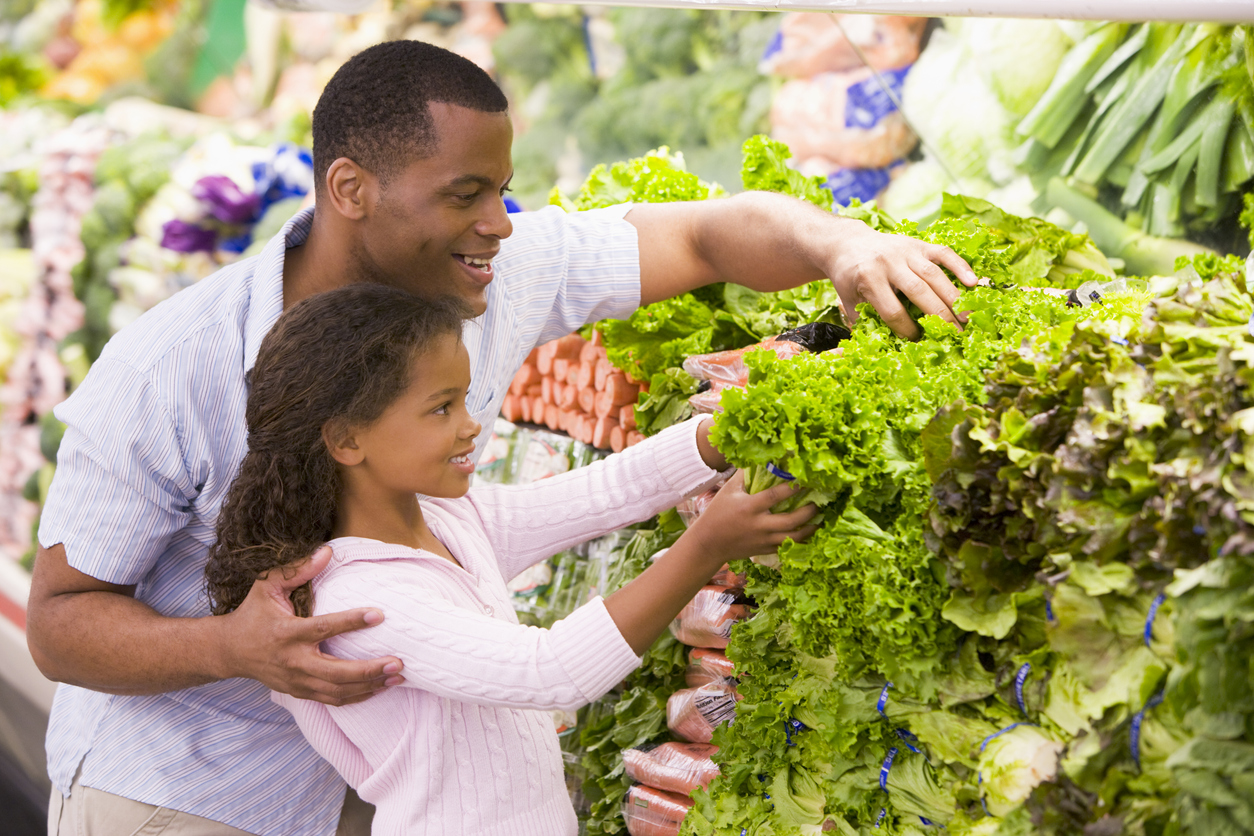 Father and daughter in supermarket produce section picking vegetables