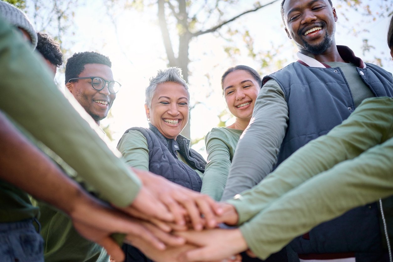 Teamwork, motivation and huddle with senior friends hiking together in the forest or woods from below. Fitness, exercise or nature with a mature man and woman friend group putting hands in a circle