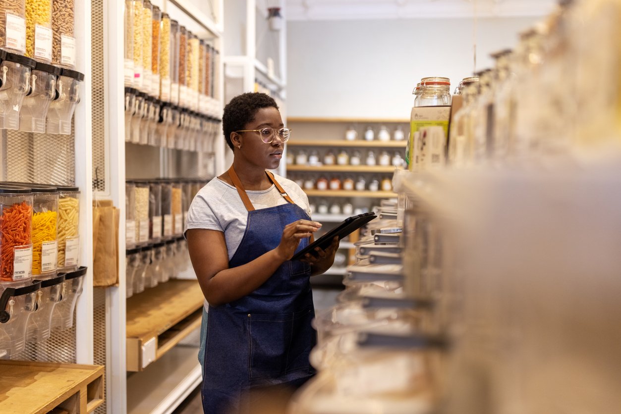 African young woman with digital tablet working at zero waste store. Female store owner checking stock in the eco-friendly grocery shop.