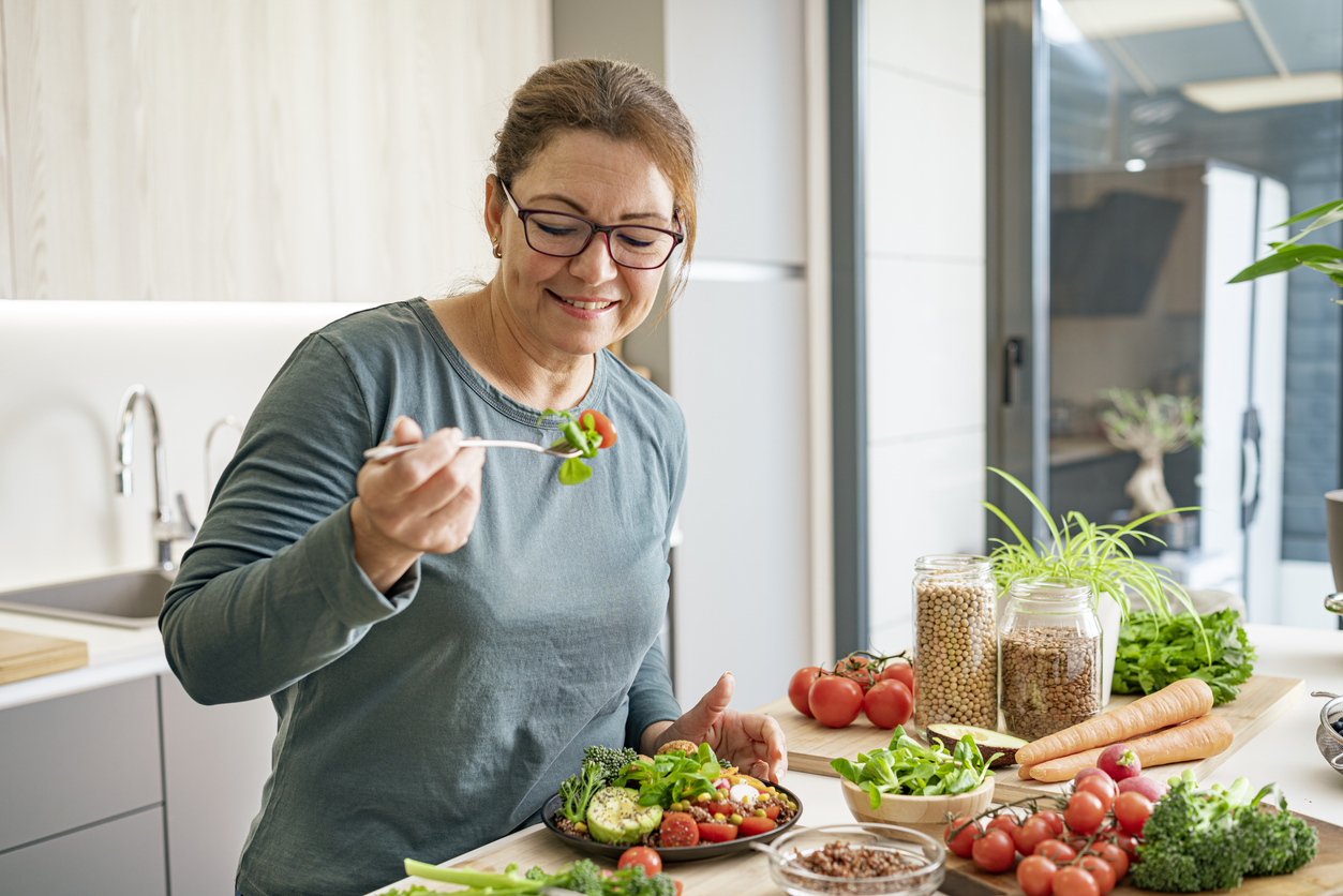 Portrait of a mature Hispanic woman eating healthy vegan salad plate in domestic kitchen. Healthy eating concept. High resolution 42Mp indoors digital capture taken with SONY A7rII and Zeiss Batis 40mm F2.0 CF lens