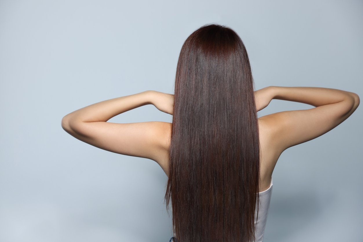 Young woman with healthy strong hair on light gray background, back view