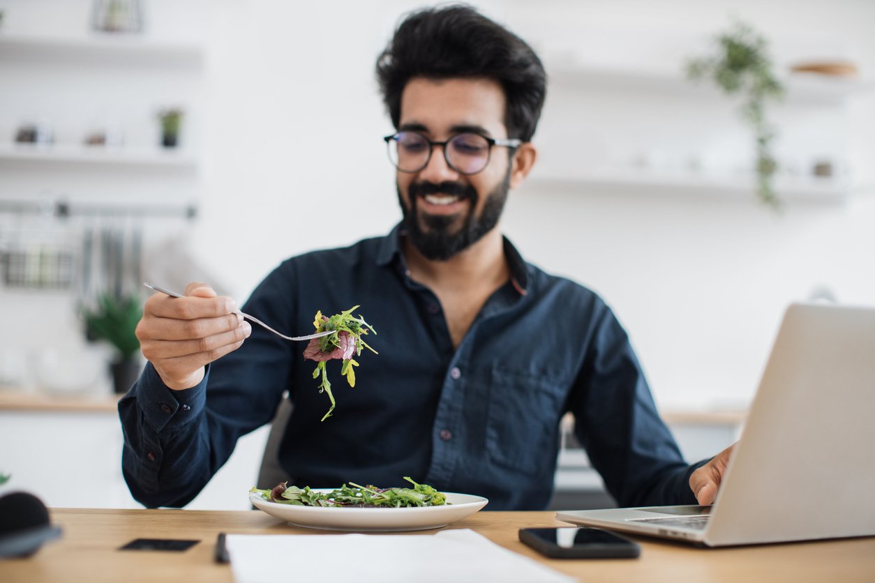 Portrait of arabian gentleman posing with vegetarian salad near computer at writing desk in home office. Cheerful business person increasing energy while choosing healthy diet in distant workplace.