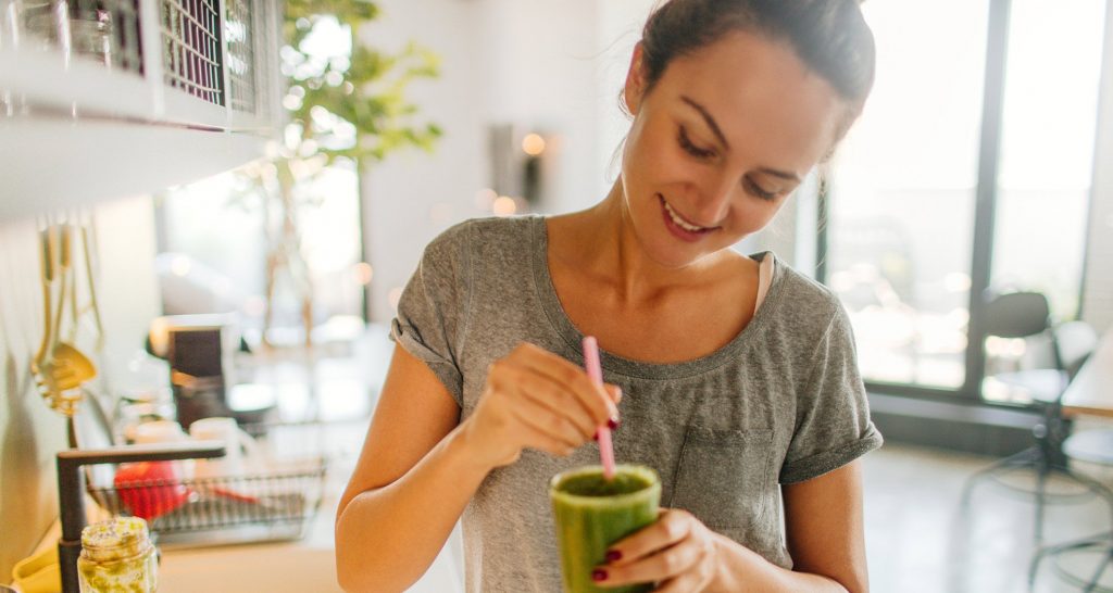 A woman stirring a green smoothie with a straw in her kitchen