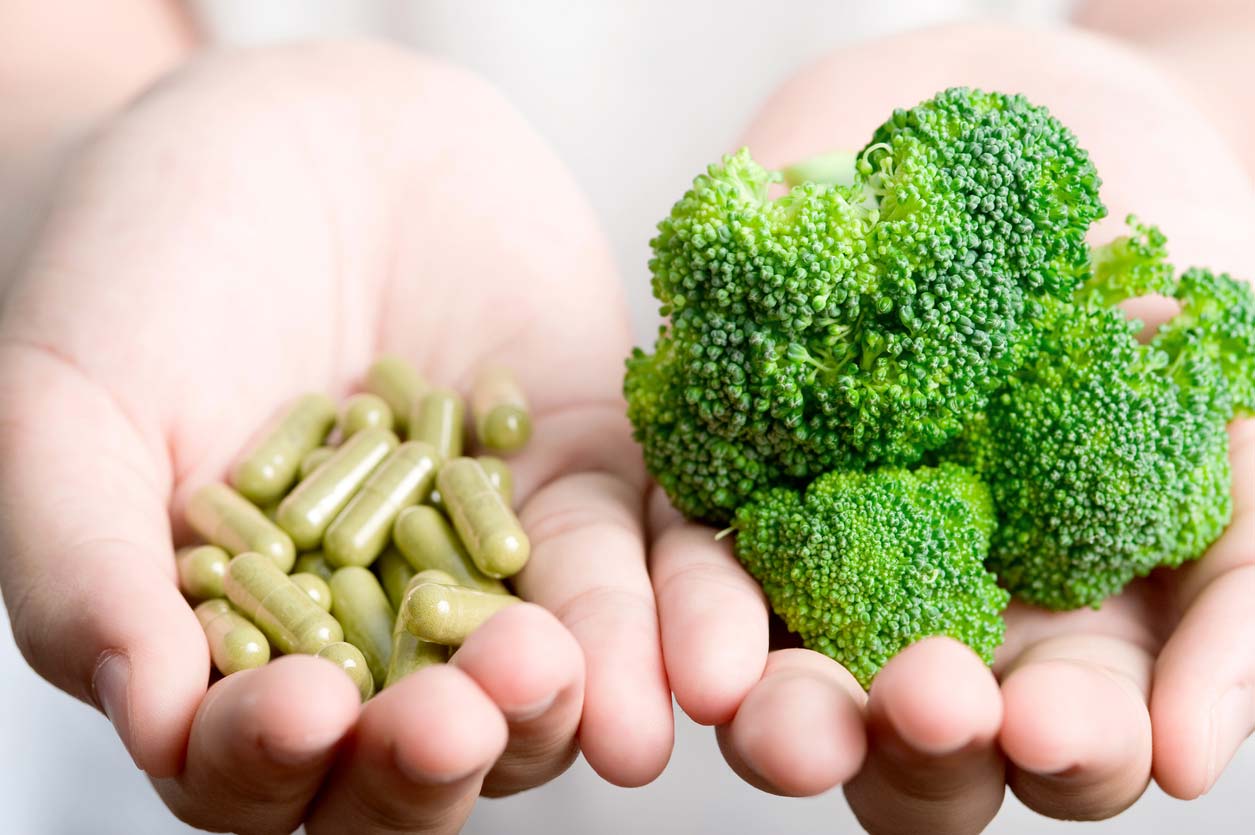 Hands holding broccoli sprouts supplements with sulforaphane and a crown of broccoli