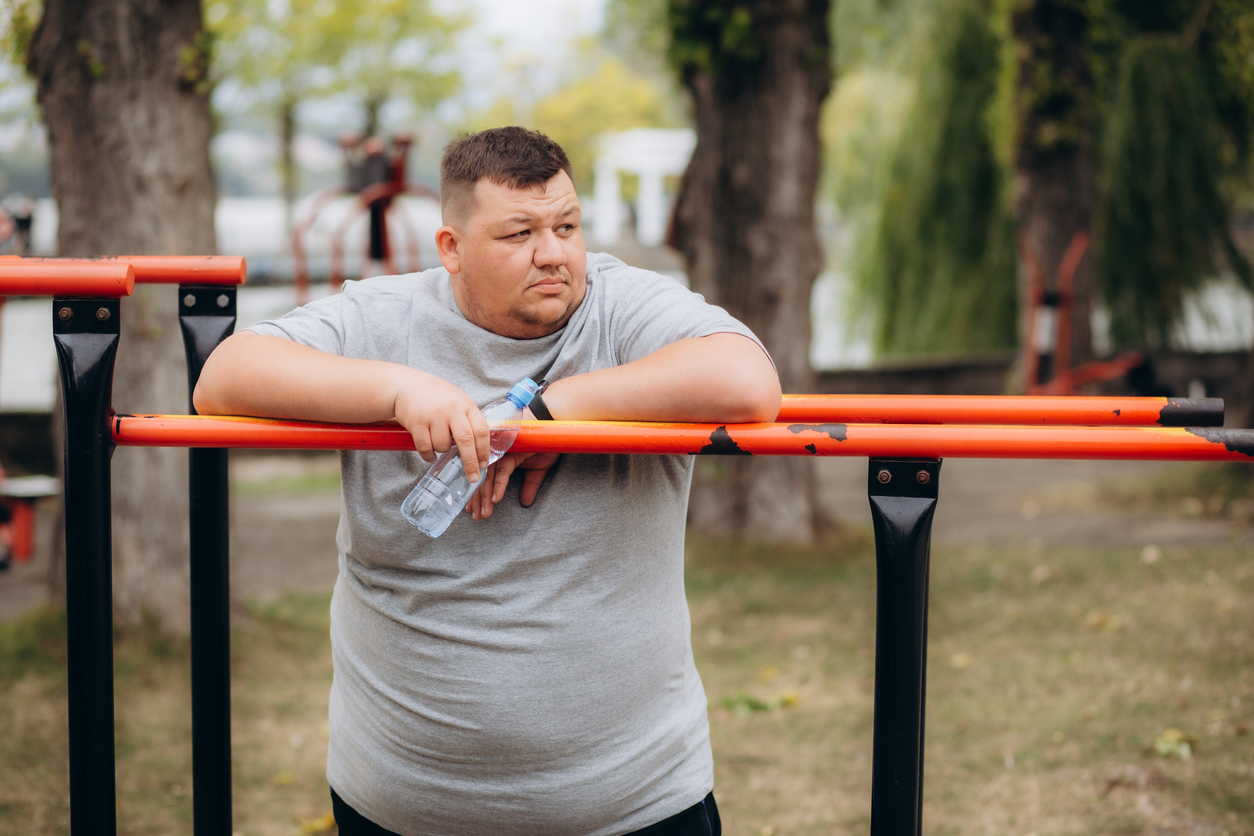 Picture of fat man looks tired while drinking a bottle of water after exercising in the park. High quality photo