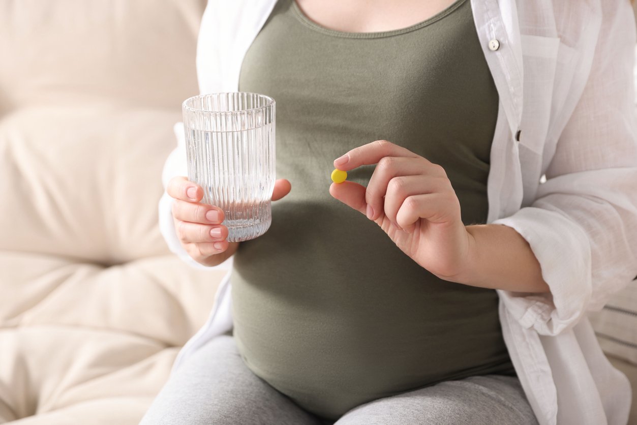 Pregnant woman holding pill and glass with water on sofa, closeup