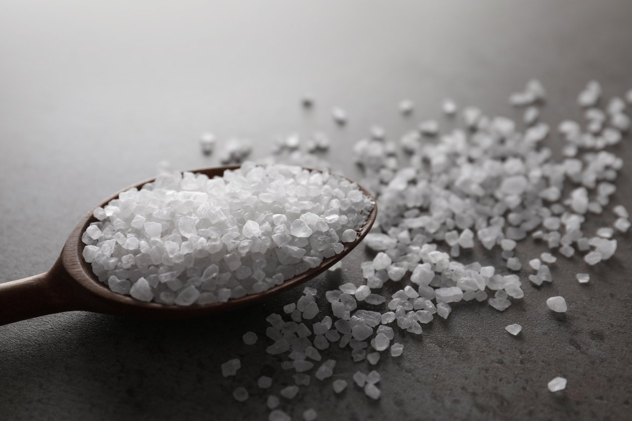 Spoon of natural sea salt on grey table, closeup