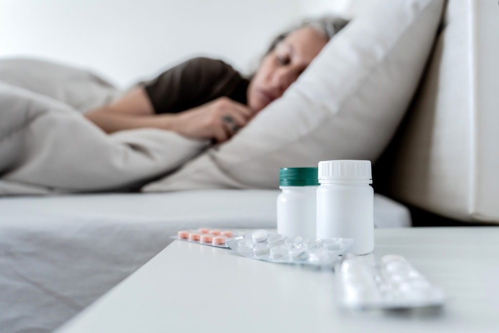 Older woman in bed with a variety of pills on the bedside table