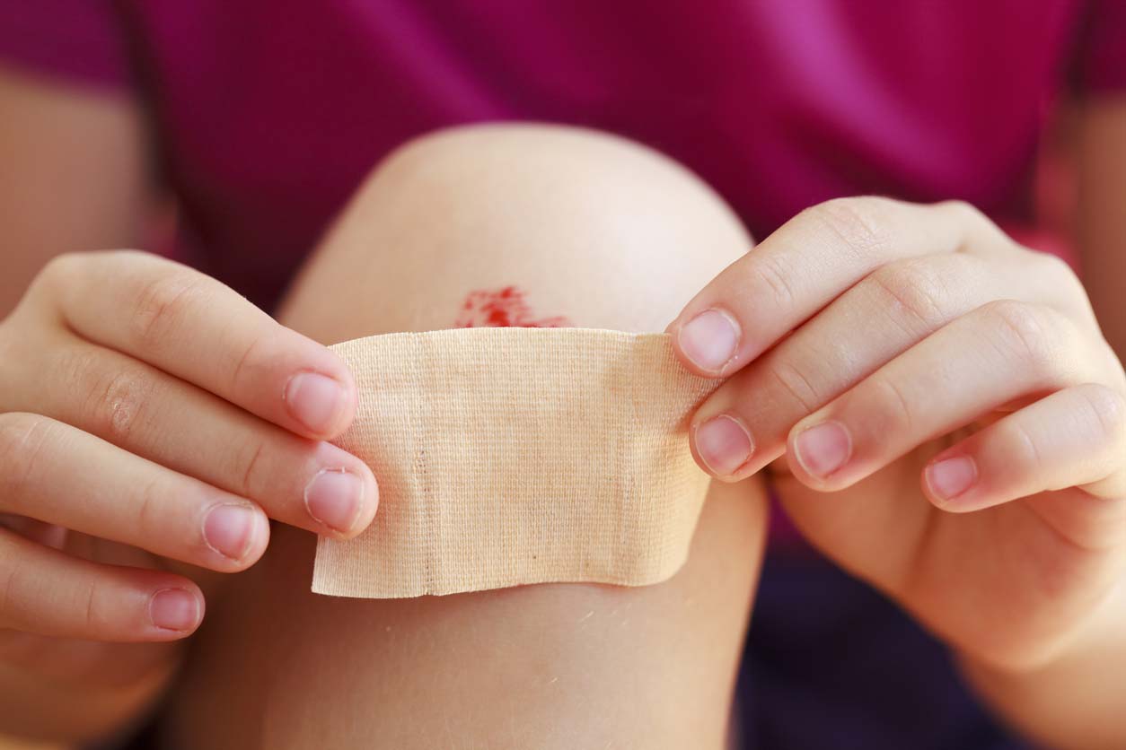 child putting bandaid over scraped knee