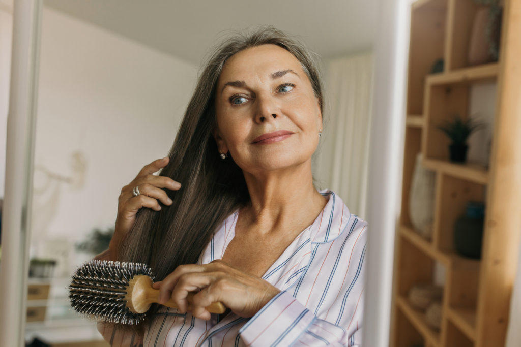 Elderly female combing grey hair with round hairbrush