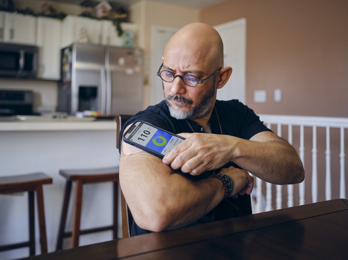 A mature hispanic man in a home, checking his blood sugar level.