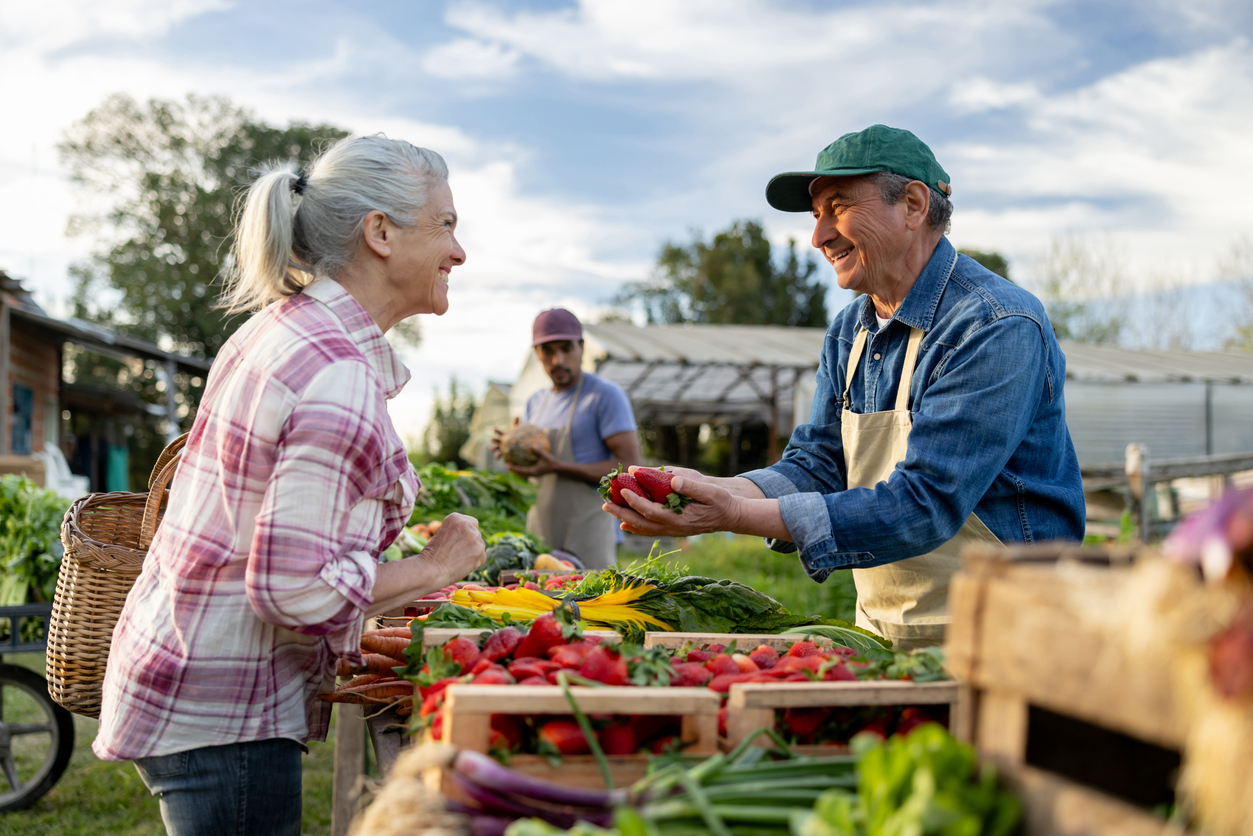 Happy Latin American farmer selling organic strawberries to a client at a Farmer's Market - small business concepts